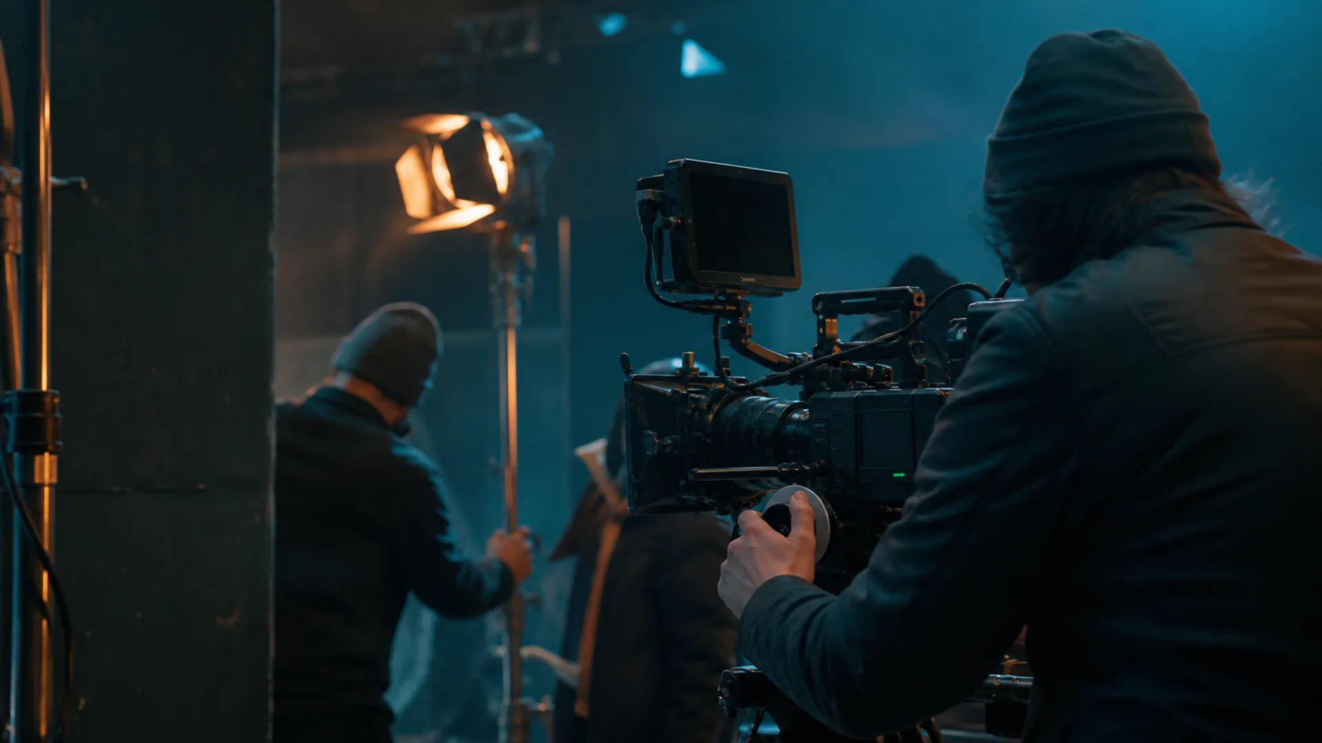 Anonymous camera operator and crew working on a blue-and-amber lit film set